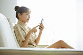 自宅で電話を操作している若いアジアの女性