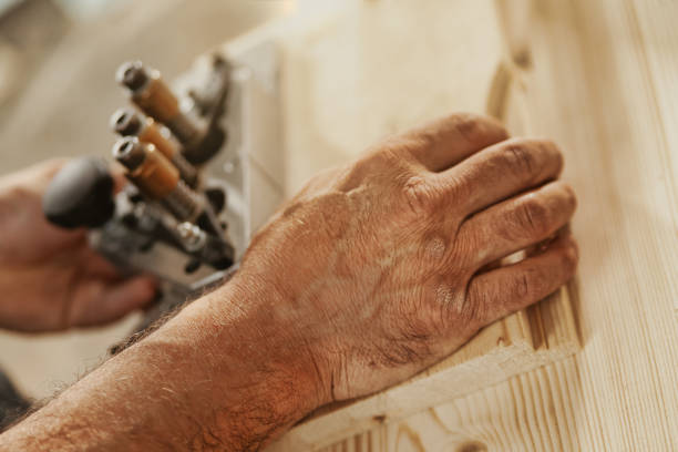 Hand of a carpenter working on cabinetry in an industrial workshop in close up as he uses machinery on a workbench