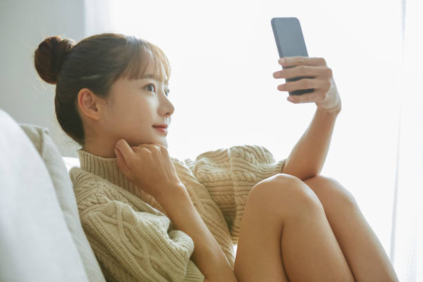 自宅で電話を操作している若いアジアの女性 - 自分撮り ストックフォトと画像