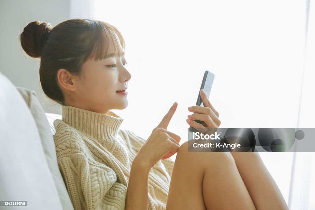 A young Asian woman operating a phone at home day time, back light Women Stock Photo