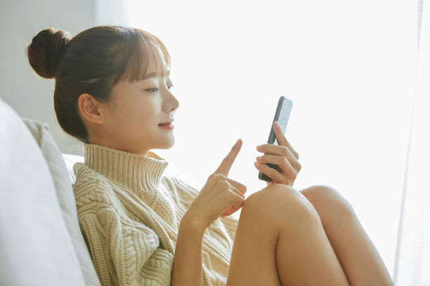 молодая азиатская женщина, управляющая телефоном дома - beautiful communication enjoyment happiness стоковые фото и изображения