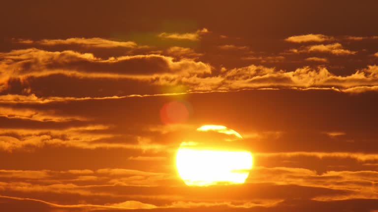 4k fast speed closeup scene by super telephoto lens on big orange color sun rise up pass through stream of dark cloud on cloudy sky