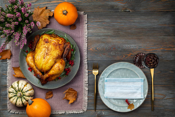 Roasted chicken or turkey for Thanksgiving Day on festive table setting with protective mask on wooden table. Fried chicken, pumpkins for Thanksgiving dinner. Concept Thanksgiving Day in pandemic covid 19 Roasted chicken or turkey for Thanksgiving Day on festive table setting with protective mask on wooden table. Fried chicken, pumpkins for Thanksgiving dinner. Concept Thanksgiving Day in pandemic covid 19 thanksgiving holiday covid stock pictures, royalty-free photos & images