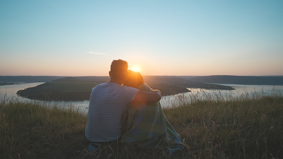 The romantic couple sitting on a mountain top on a beautiful sunset background