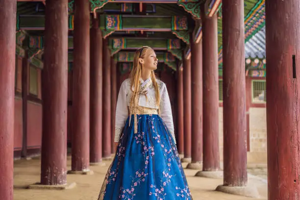 Young caucasian female tourist in hanbok national korean dress at Korean palace. Travel to Korea concept. National Korean clothing. Entertainment for tourists - trying on national Korean clothing.