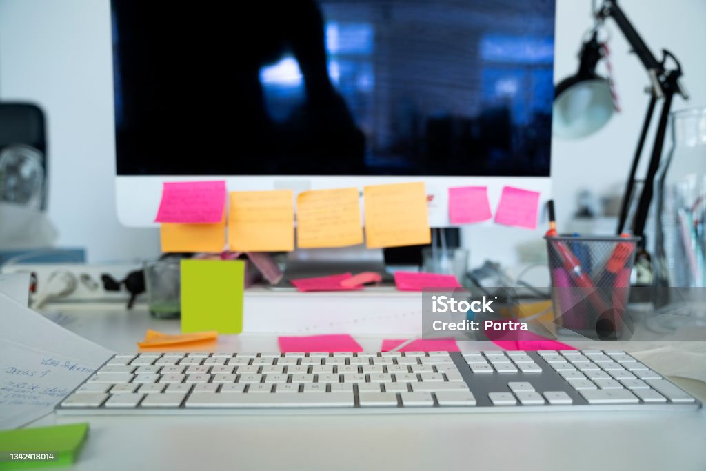 Messy workstation in office with sticky notes on computer monitor Messy office table top with many sticky notes on computer monitor and desk. Close-up of a busy workstation in office. Desk Stock Photo