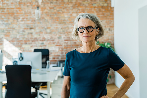 Portrait of a senior woman standing in office. Female entrepreneur with short hair and business casuals looking at camera.