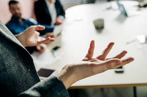 Close-up of female professional making hand gestures while giving presentation in meeting. Businesswoman addressing team sitting at conference table in office.