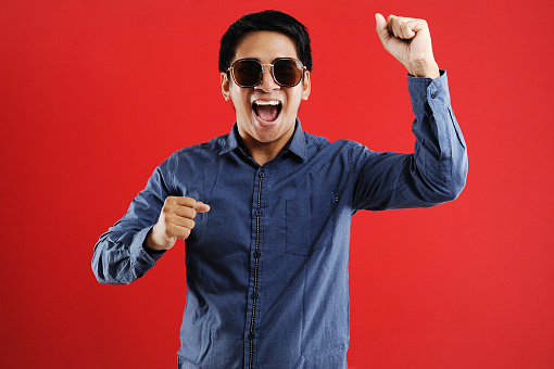 Young asian man happy and excited expressing winning gesture. Successful and celebrating on red background