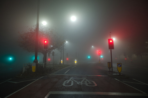 Colored traffic lights and white street lamps shine through thick fog