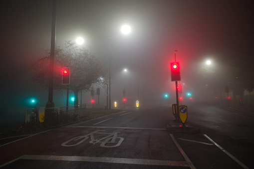 Extremely foggy night time conditions at a junction of two english B roads. Many traffic lights and street lights shine through the atmospheric haze