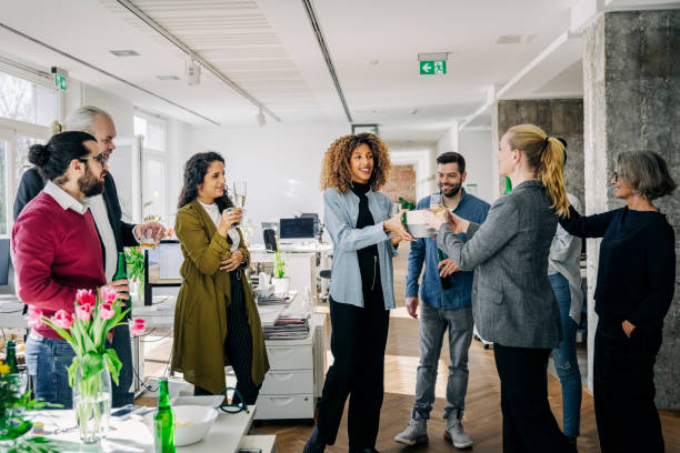 Businesspeople giving a farewell party of a female colleague in office Businesswoman receiving a gift from female colleague during party. Business professionals giving a farewell party of a female colleague in office. business gifts stock pictures, royalty-free photos & images