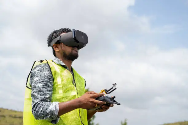 Photo of Professional drone pilot controlling drone by looking into virtual reality headset using remote controller - Concept of modern Surveillance technology and inspection