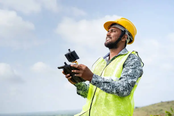 Photo of Drone pilot with safety helmet operating drone using remote controller - concept of engineer using drone technology to survey land.