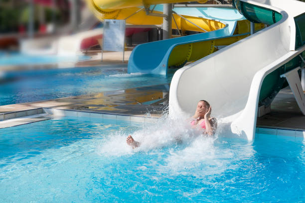 water slides, a woman with splashes and laughter plops into the water, summer entertainment on vacation at the hotel stock photo