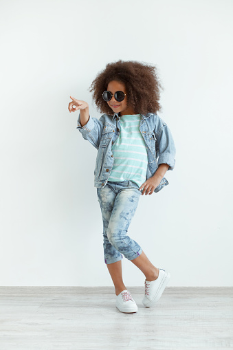 Funny stylish girl with beautiful curly hair wearing denim clothes and sunglasses