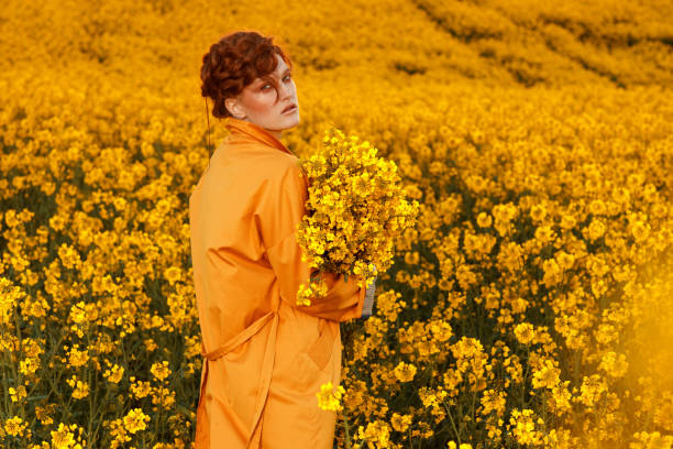 portrait de femmes aux cheveux roux vêtues d’un trench-coat orange d’automne tendance dans un champ orange coloré. vêtements de mode look d’automne - ethnic editorial make up colors photos et images de collection