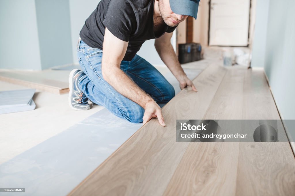 Work of a master floating flooring installation - installing laminate on the floor Close-up of the work of a master floating flooring installation - installing laminate on the floor - male hands during work Flooring Stock Photo