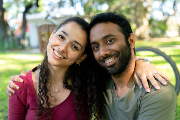 istock Beautiful diverse couple at the park on a sunny day facing camera smiling while hugging each other close 1342431894