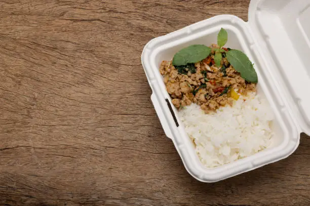 Photo of Spicy minced pork basil topping with rice in bagasse lunch box on wooden background