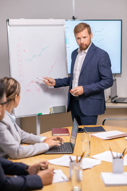 istock Young serious businessman pointing at graph on whiteboard 1342438522