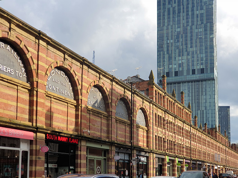Manchester, United Kingdom - August 9, 2021: View of the classical brick houses on Deansgate street with the Hilton Manchester Deansgate skyscraper in the background. Deansgate is one of the city's oldest thoroughfares.
