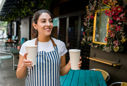 Portrait of a happy Latin American waitress working at a cafe serving drinks and smiling - food service concepts