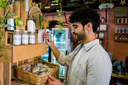 Happy Latin American man shopping at an organic market and looking at a bottle of supplements -healthy lifestyle concepts