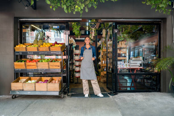 femme heureuse travaillant dans un marché alimentaire local et se tenant à la porte en attendant les clients - market stall photos et images de collection