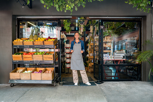 Happy woman working at a local food market and standing at the door waiting for clients