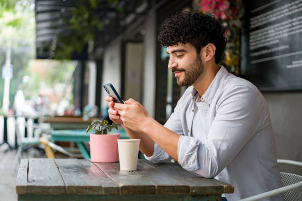 Happy man drinking checking his cell phone at a coffee shop while drinking a cappuccino stock photo