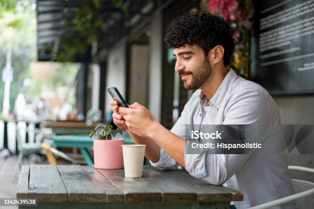 Happy Man Drinking Checking His Cell Phone At A Coffee Shop While Drinking A Cappuccino Stock Photo - Download Image Now