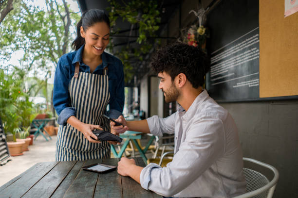 Man making a contacless payment at a restaurant using his cell phone Latin American man making a contacless payment to the waitress at a restaurant using his cell phone paid stock pictures, royalty-free photos & images