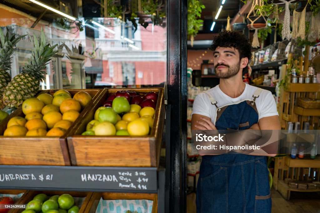 Man working at a local supermarket and waiting for clients Latin American man working at a local supermarket and waiting for clients at the door - essential services concepts Supermarket Stock Photo