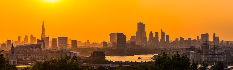 Orange sun setting over the iconic skyscraper skyline of central London and the River Thames, UK.