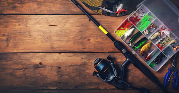 fishing tackle - spinning rod with box of lures and equipment on wooden background. copy space - haak apparatuur stockfoto's en -beelden