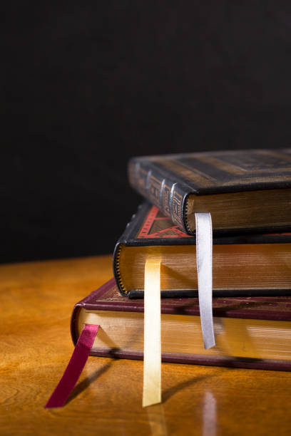 Stack of  beautiful leather bound books.  Highly polished wood table.  Black background.  Satin ribbon bookmarks.  Room for copy.