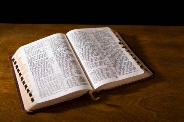 istock Open book or Bible on highly polished wood table.  Black background.  Reflection in table and there is a satin bookmark inside the book. 1342443989