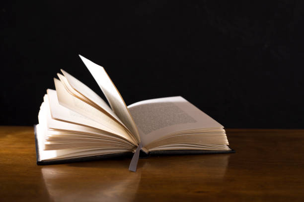 istock Open book or Bible on highly polished wood table.  Black background. 1342444036