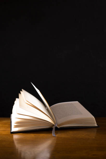 istock Open book or Bible on highly polished wood table.  Black background. 1342444052