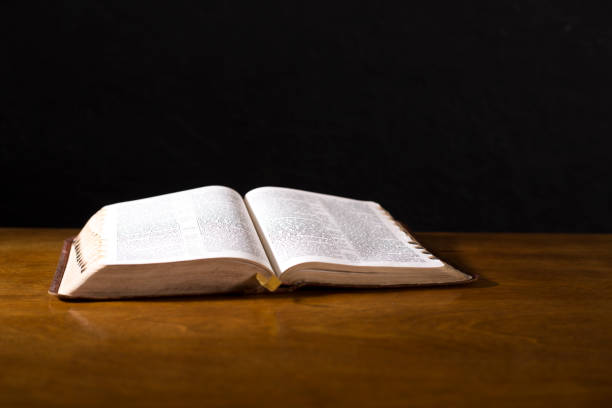 istock Open book or Bible on highly polished wood table.  Black background. 1342444064