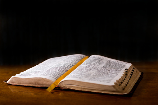 Open book or Bible on highly polished wood table.  Black background.  Reflection in table and there is a satin bookmark inside the book.  Tabs along side for ease of referencing.