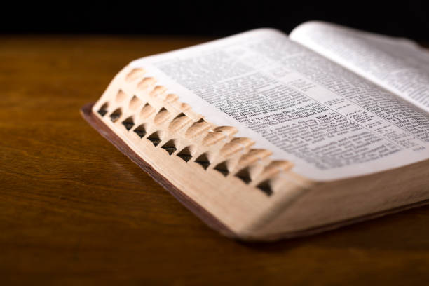 istock Open book or Bible on highly polished wood table.  Black background. 1342444097