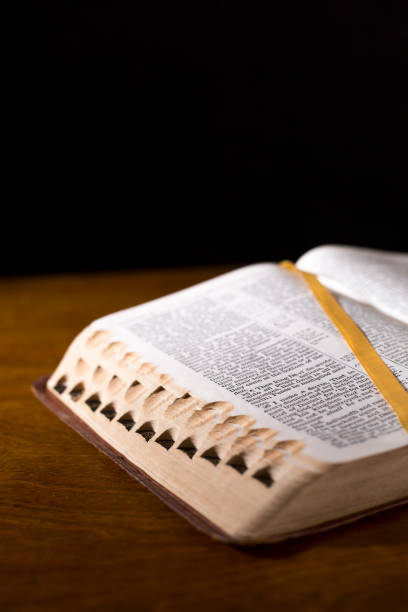istock Open book or Bible on highly polished wood table.  Black background. 1342444121