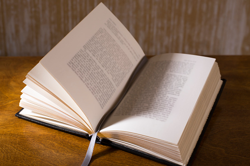 Open book or Bible on highly polished wood table.  Black background.  Reflection in table and there is a satin bookmark inside the book.