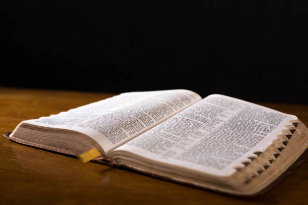 istock Open book or Bible on highly polished wood table.  Black background. 1342448281