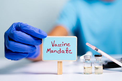 Concept of coronavirus or covid-19 vaccine mandate, showing with doctor hands with gloves by placing sign board next to vaccine shots and syringe