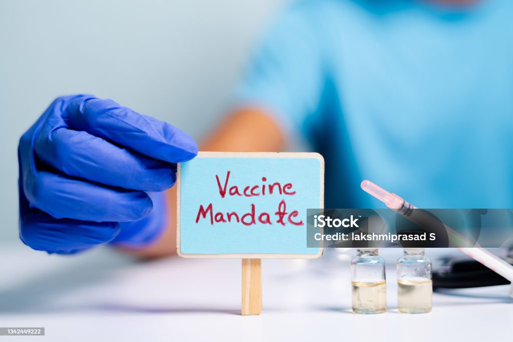 Concept of coronavirus or covid-19 vaccine mandate, showing with doctor hands with gloves by placing sign board next to vaccine shots and syringe Concept of coronavirus or covid-19 vaccine mandate, showing with doctor hands with gloves by placing sign board next to vaccine shots and syringe. Vaccination Stock Photo