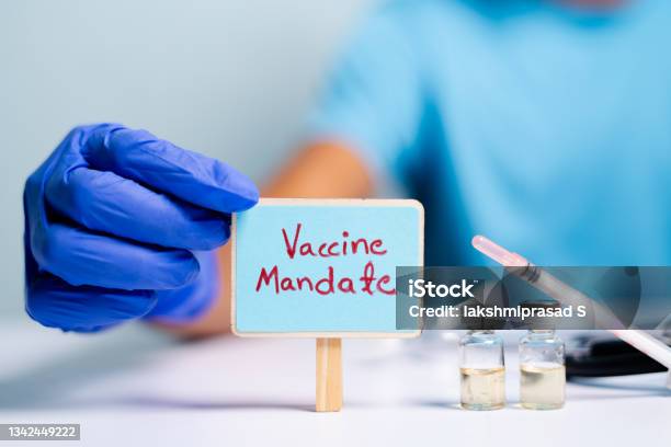 Concept Of Coronavirus Or Covid19 Vaccine Mandate Showing With Doctor Hands With Gloves By Placing Sign Board Next To Vaccine Shots And Syringe Stock Photo - Download Image Now