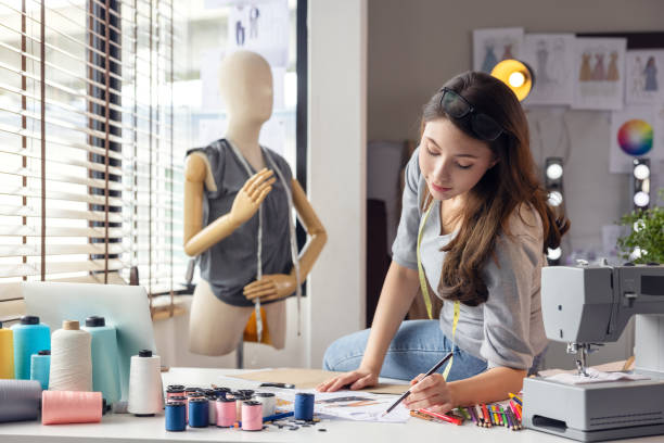 istock performance at clothes in the background, a professional tailor designer makes notes and drawings in a notebook, Business Owner With Tape Measure Working In Fashion Sitting On Desk